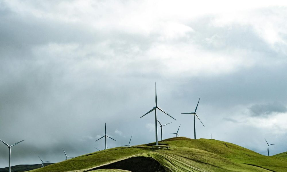 Wind turbines on lush hills with a dramatic cloudy sky, symbolizing clean energy and sustainability.
