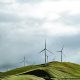 Wind turbines on lush hills with a dramatic cloudy sky, symbolizing clean energy and sustainability.